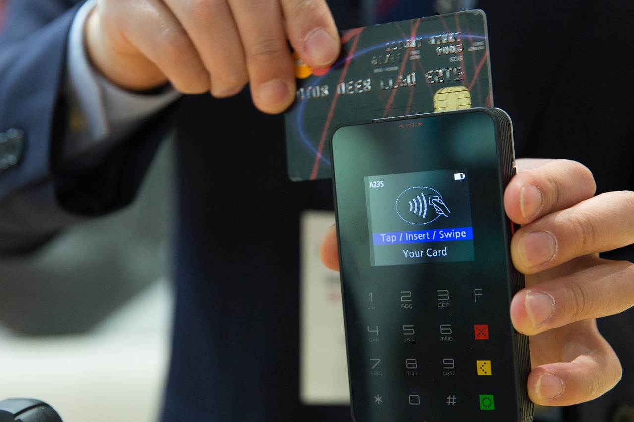 A close-up image of a person holding a card reader with payment instructions on display and swiping a payment card through it.