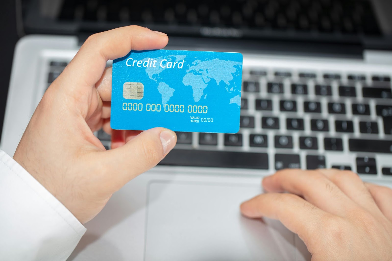 An image of a hand holding a blue credit card over a laptop keyboard.