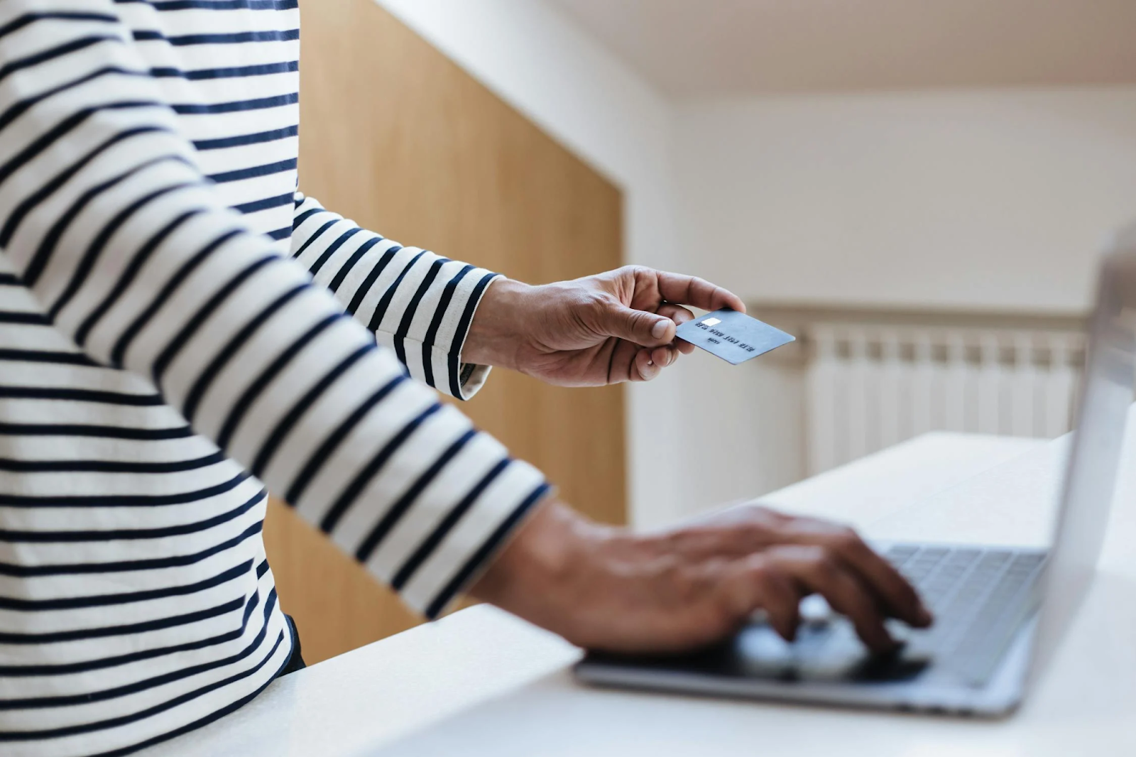 A photo of a person typing on a keyboard with one hand while holding a credit card with the other.