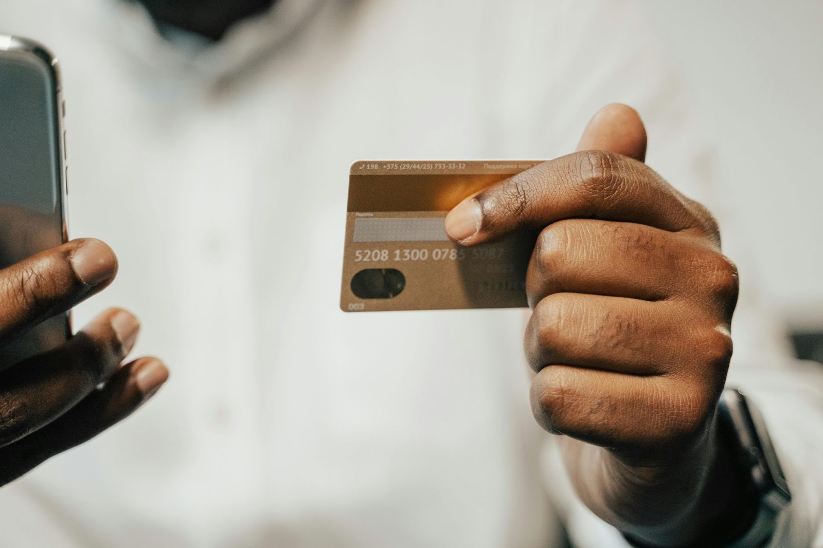 A photo of a person in a white shirt, holding a payment card in one hand and a smartphone in the other