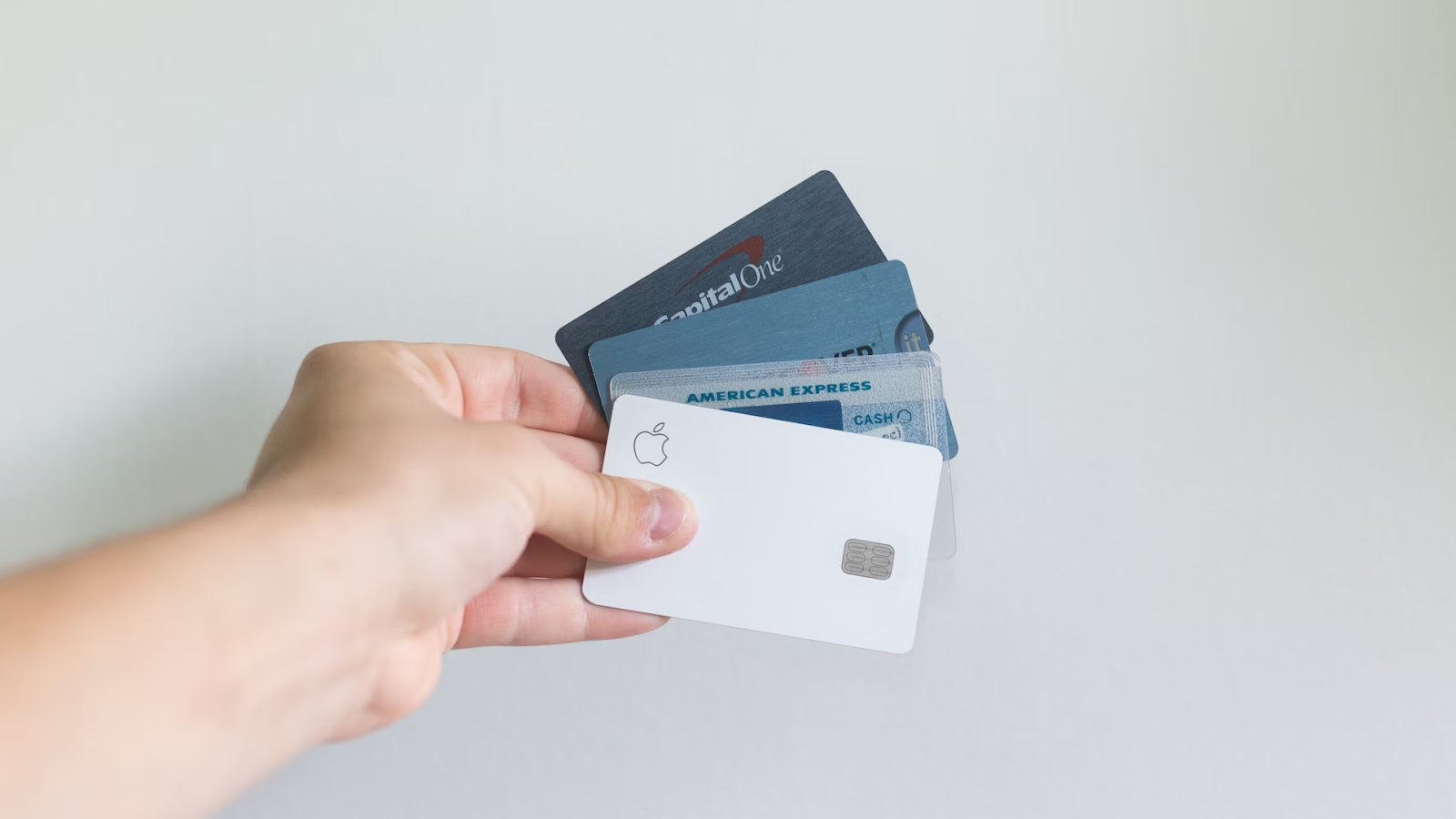 A close-up photo of a hand holding four credit cards against a gray background