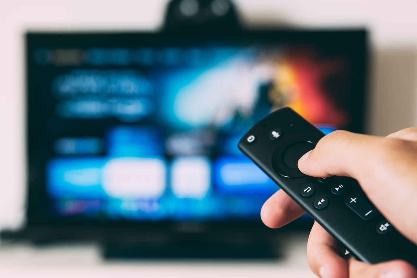 A close-up photo of a person holding a remote control pointed at the blurred TV