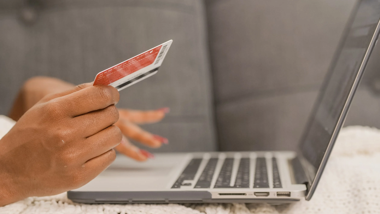 A photo of a person holding a credit card in one hand while typing on a laptop with the other