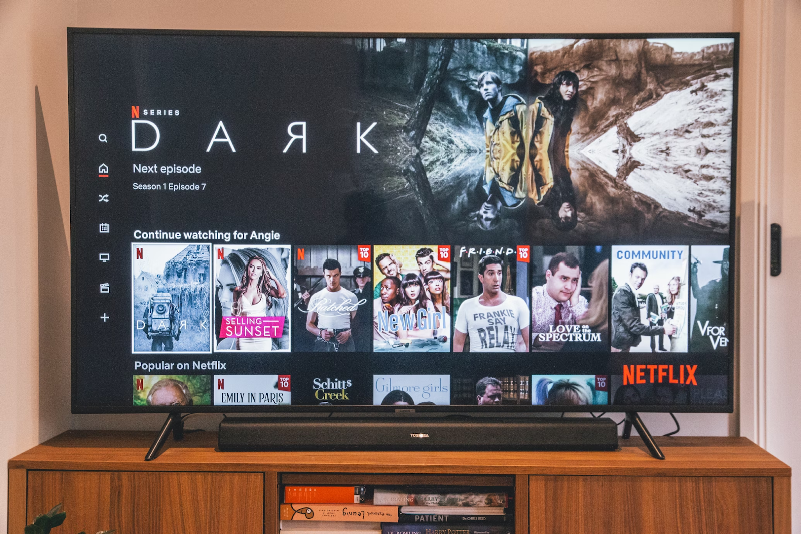 A photo of a flat-screen TV placed on a wooden stand and displaying movies and shows on Netflix