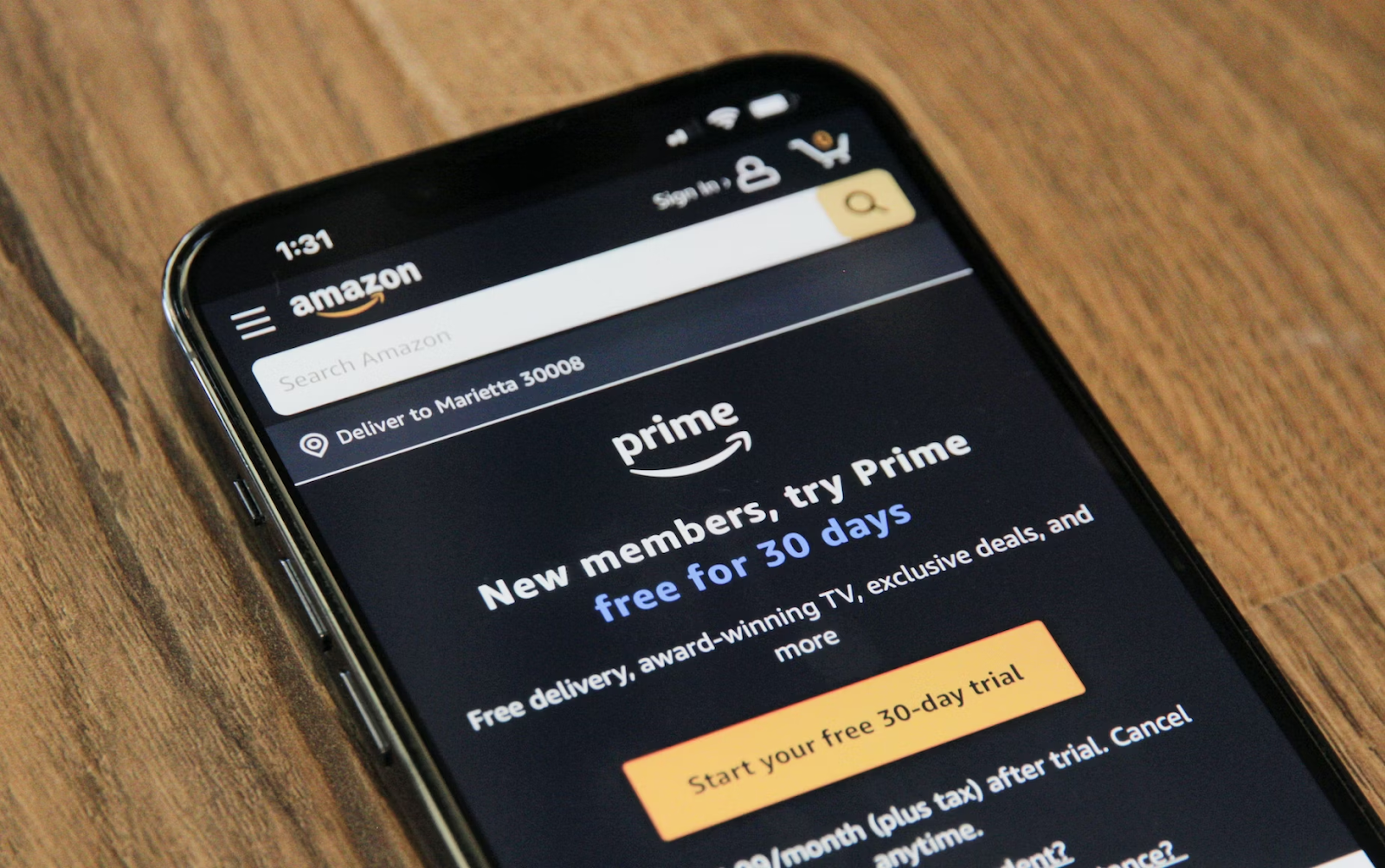 A close-up photo of a mobile phone placed on a wooden table displaying the Amazon Prime website