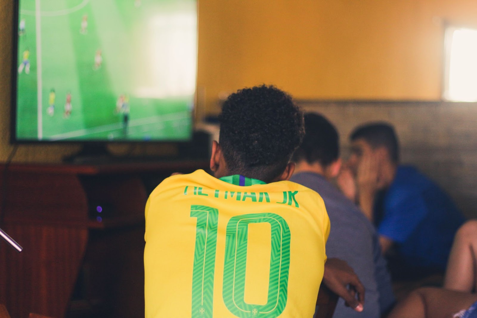 A back-shot photo of a person in a jersey watching a football match