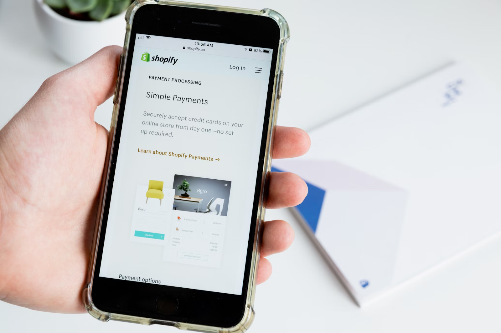 A close-up photo of a hand holding a smartphone that’s displaying Shopify’s website