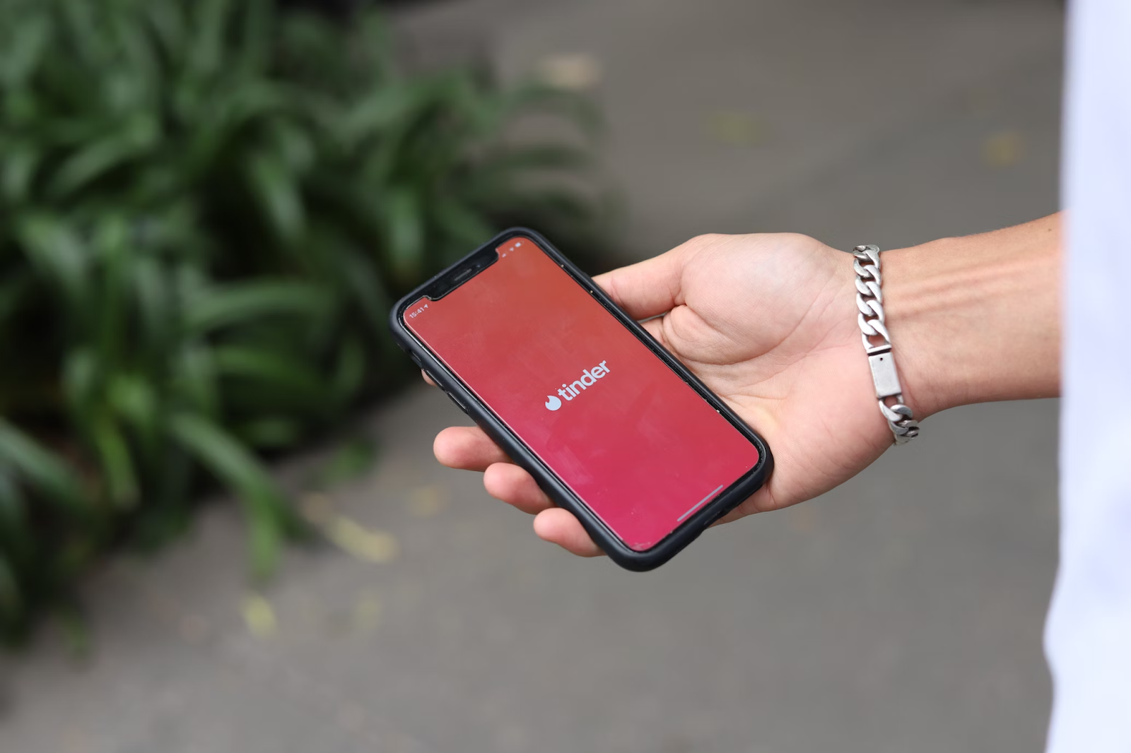 A close-up photo of a person holding a phone displaying the Tinder logo