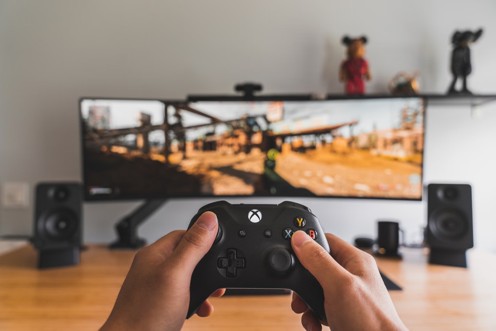 A close-up photo of a person holding a black Xbox console while playing a game on a computer