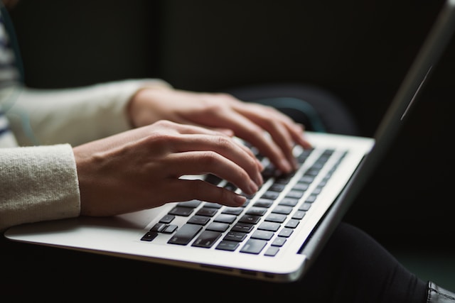 A photo of a person in a white sweater typing on a laptop keyboard