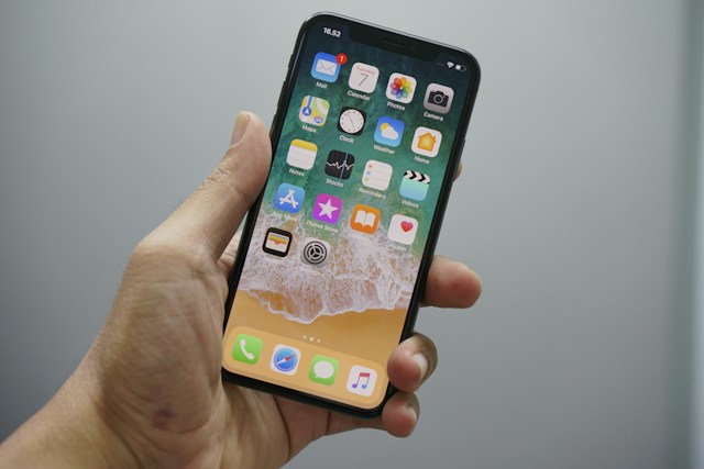 A photo of a hand holding an iPhone with a visible home screen