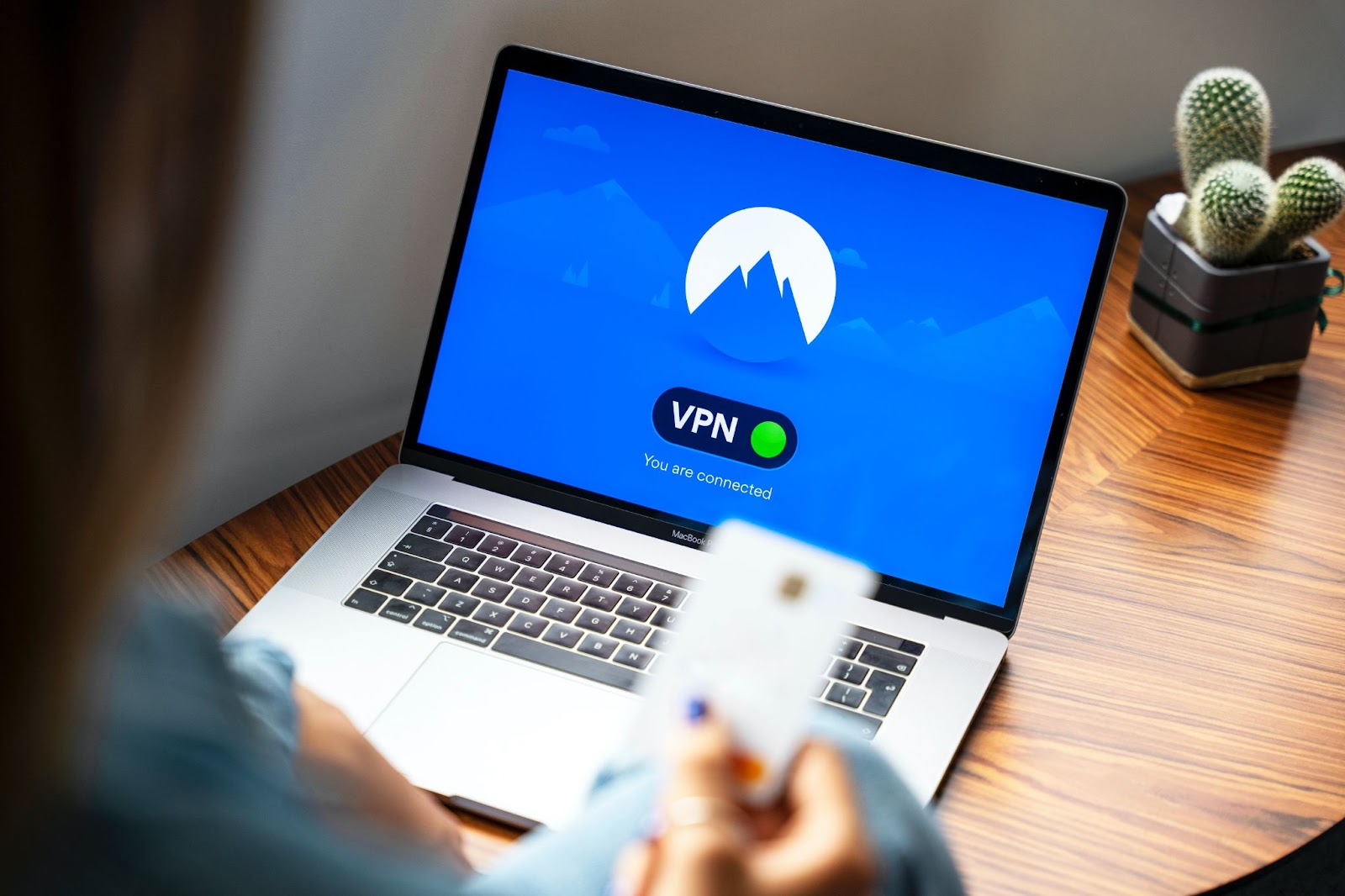 A photo of a person using NordVPN on a laptop while holding a payment card