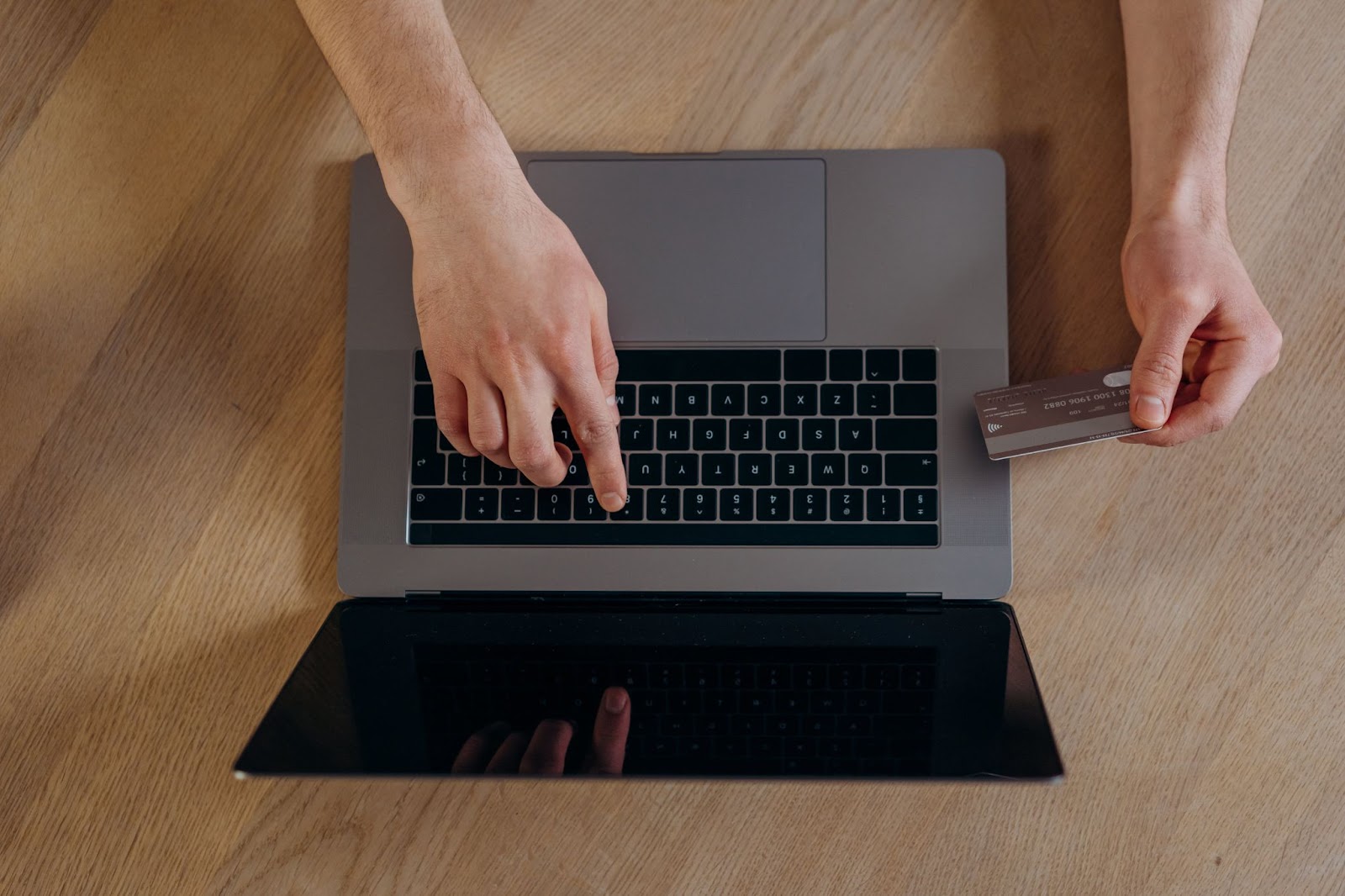 A bird’s eye view photo of a person typing payment card numbers on a Mac laptop