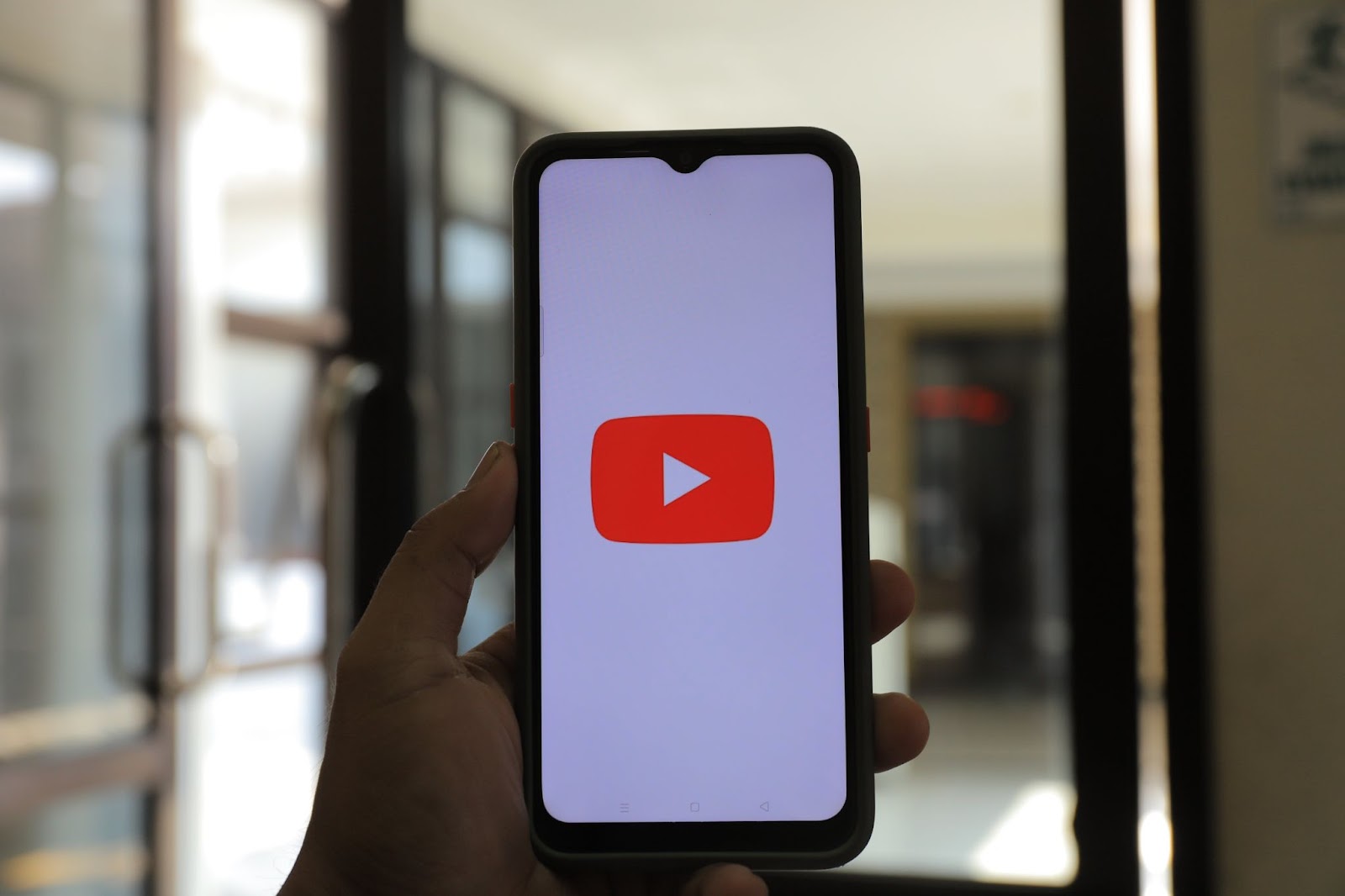 A photo of a person holding a smartphone displaying YouTube’s start screen