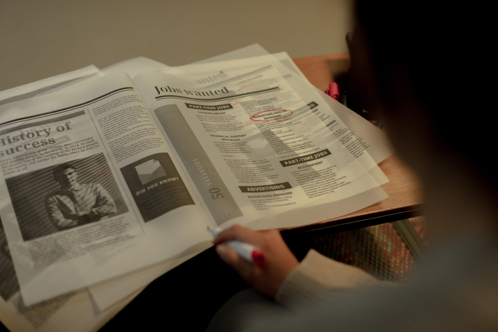 A photo of a person marking info in a newspaper placed on a table