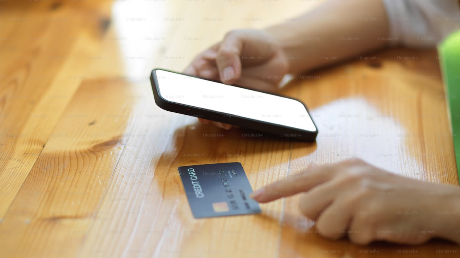 A photo of a person holding a smartphone and pointing at a payment card placed on the table