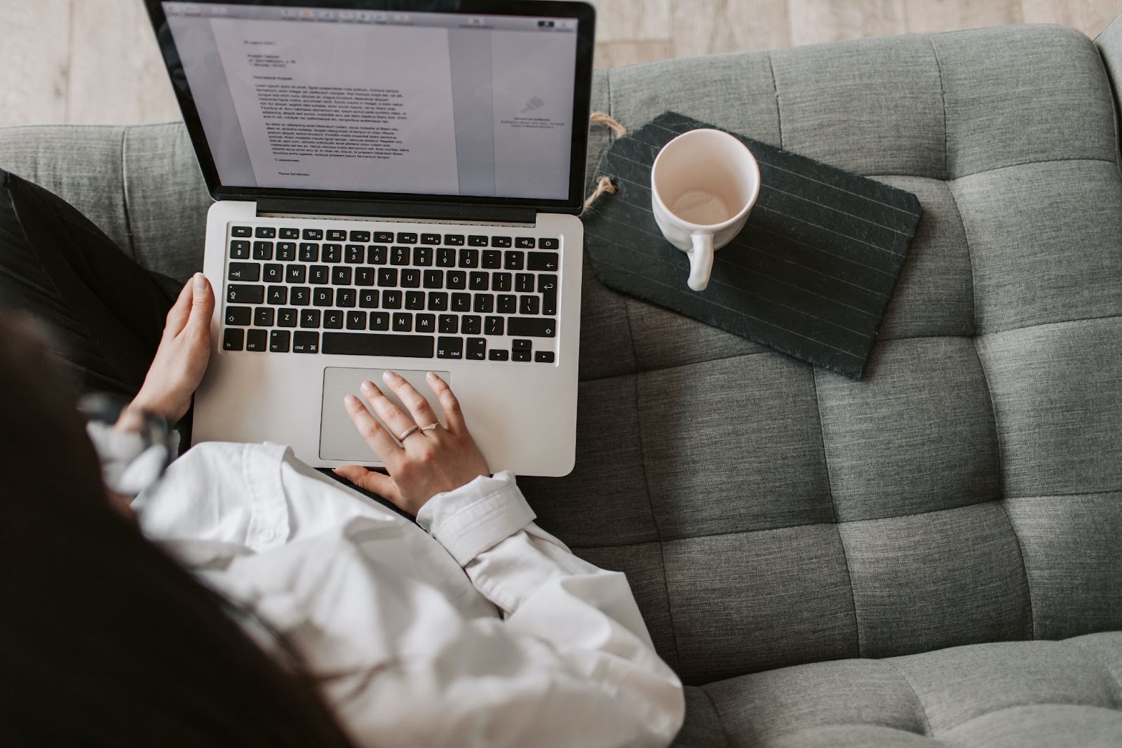 A bird's eye view photo of a person reading a document on a laptop while sitting on a couch