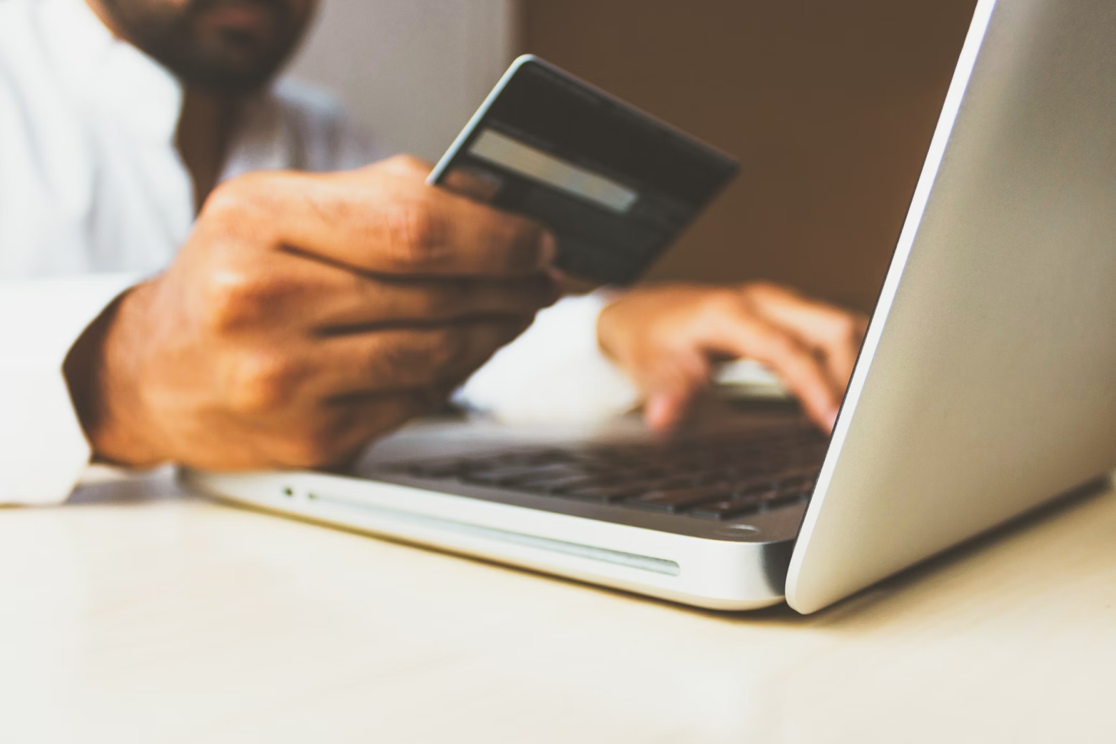 A close-up photo of a person using a laptop while holding a payment card 