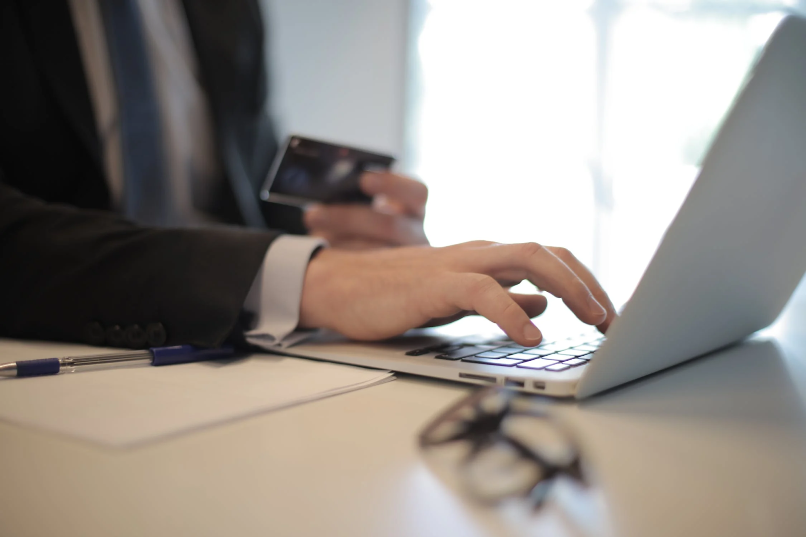 A photo of a person typing on a computer placed on a table while holding a payment card