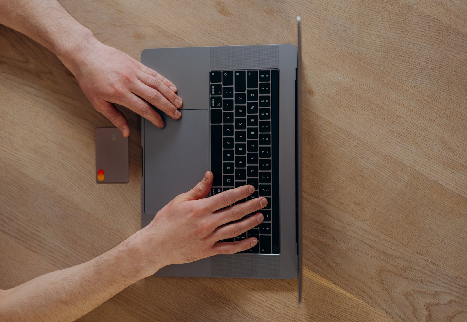 A bird's eye view photo of a person using a laptop beside a payment card placed on a wooden table