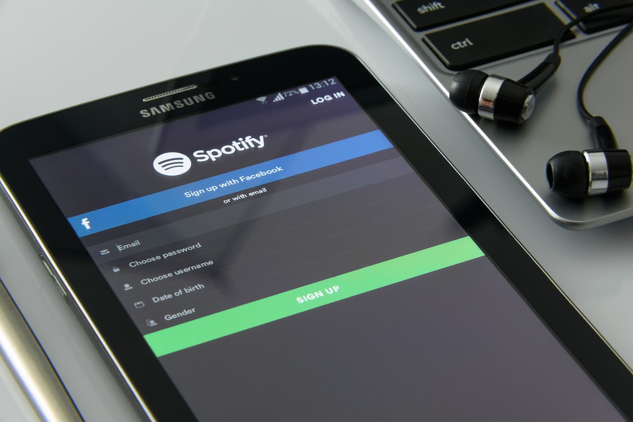 A close-up photo of a smartphone with Spotify’s signup page on the screen and earphones on the side