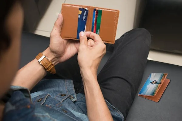 A close-up shot of a man holding a brown wallet with credit cards