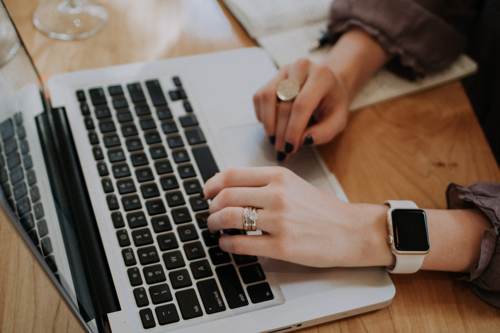 A photo of a seated person using a Macbook placed on a wooden table