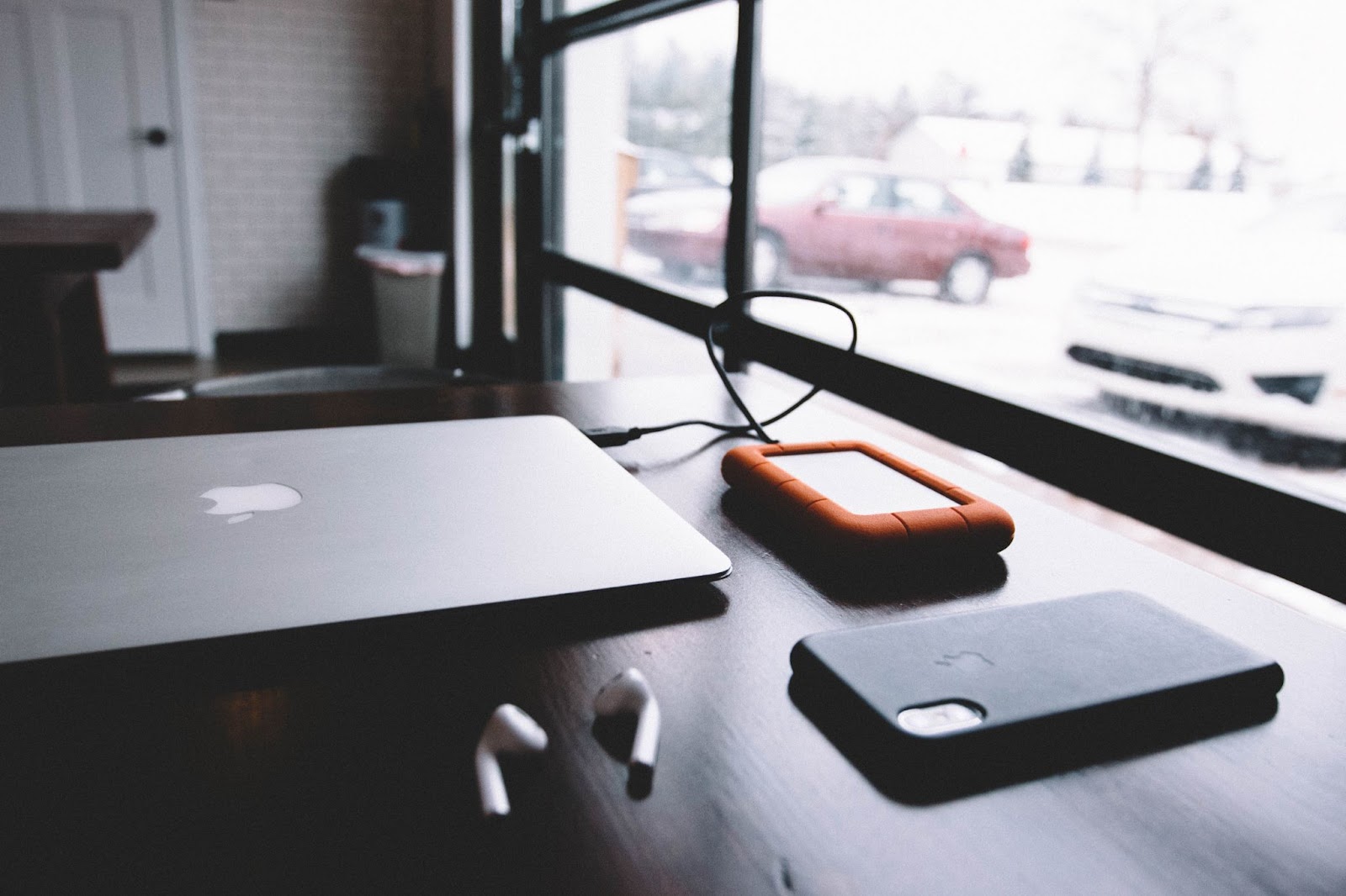 A photo of a MacBook, iPhone, and EarPods sitting on a wooden desk