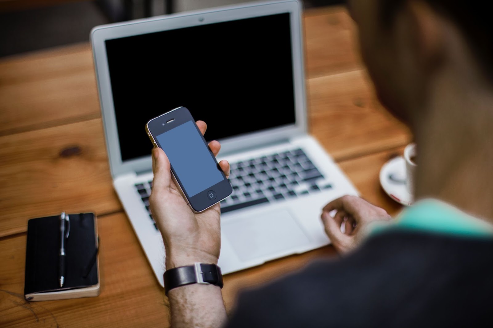 A photo of a person looking at an iPhone with a MacBook in the background