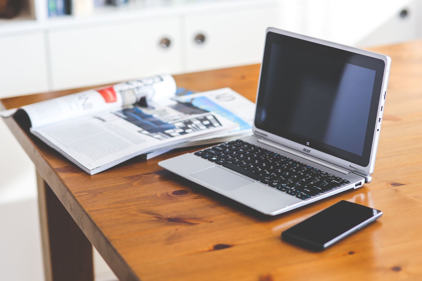 A photo of a laptop, smartphone, and some magazines on a wooden desk