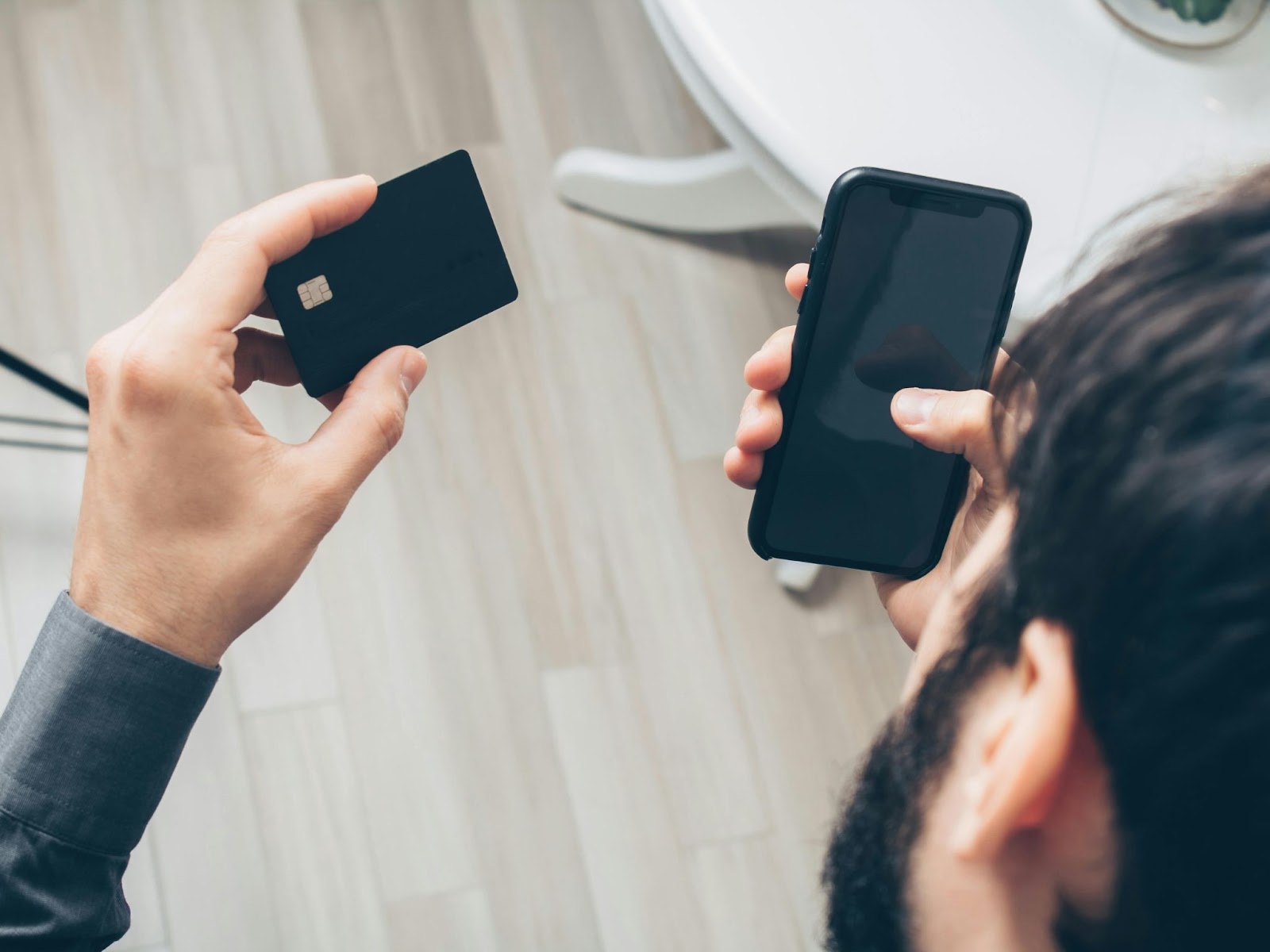 A photo of a person holding a smartphone in one hand and a payment card in the other