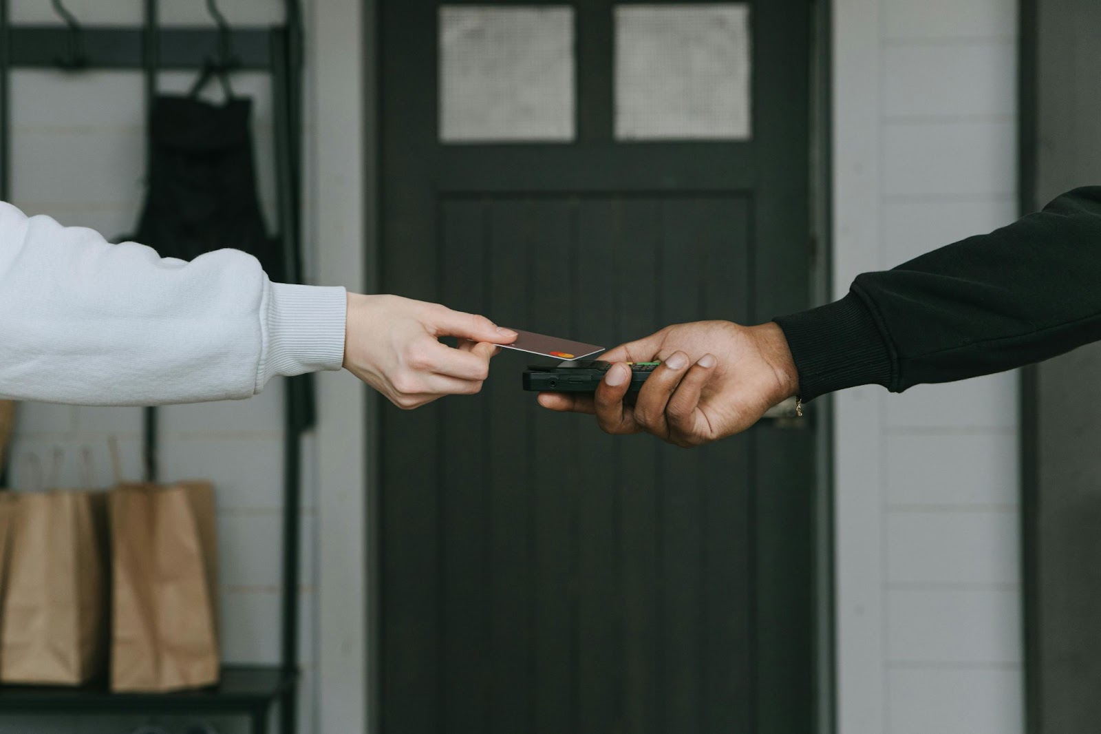 An image of two individuals' hands, with one holding a card reader and the other swiping a card over it