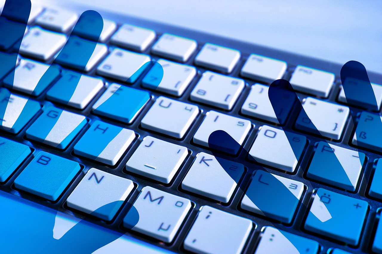 An image of a computer keyboard illuminated with blue lighting, with the shadow of a person's hands visible on the keys