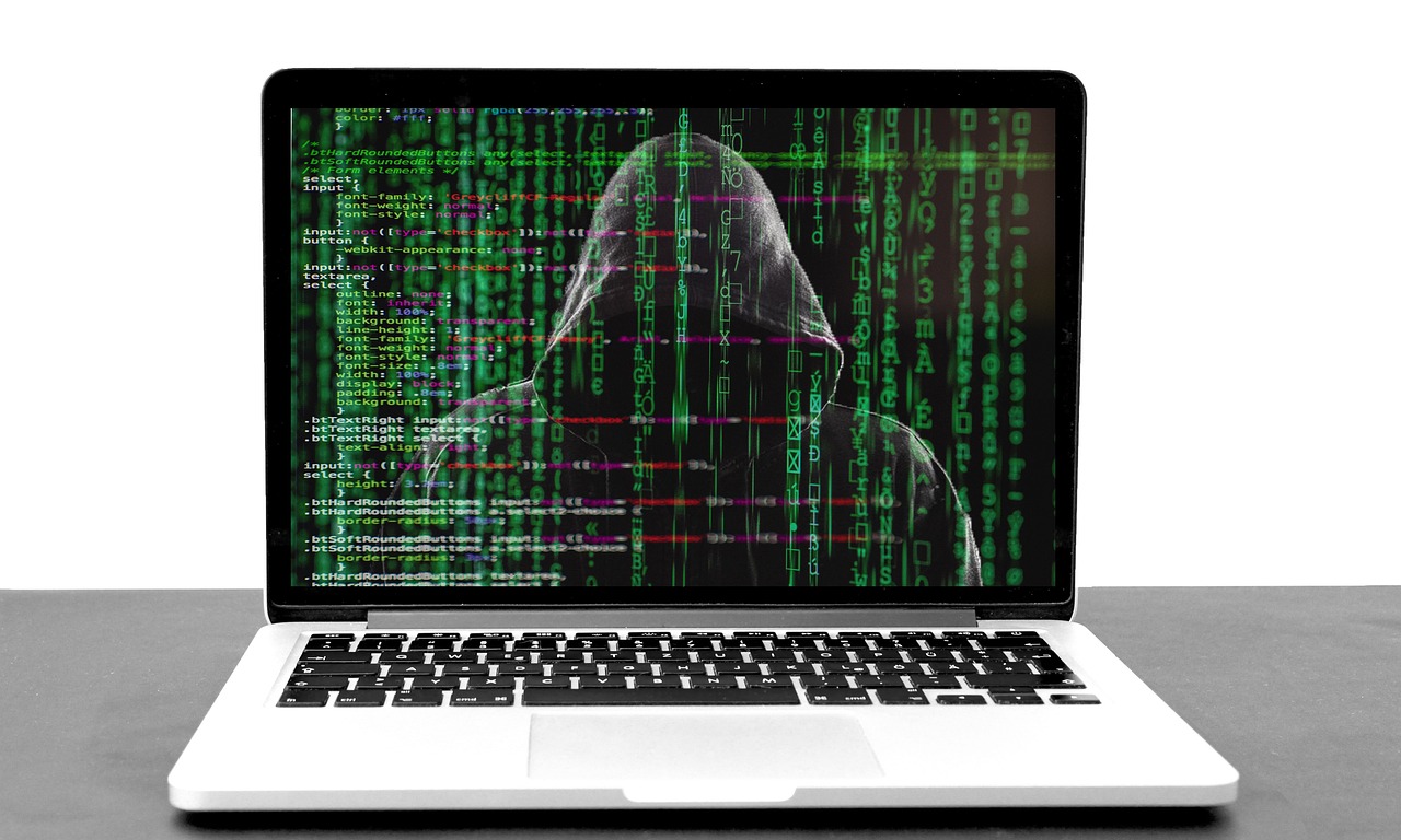 A laptop screen displaying an image of a hooded figure with green binary code overlaying it