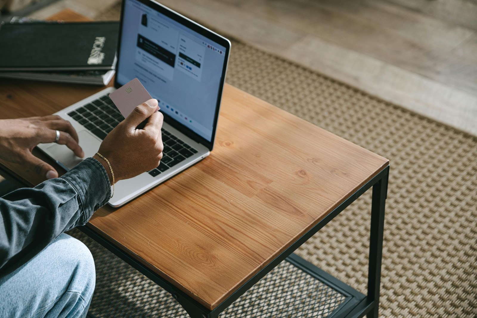 A photo of a person looking at the payment card in one hand while browsing on an open laptop resting on a small table