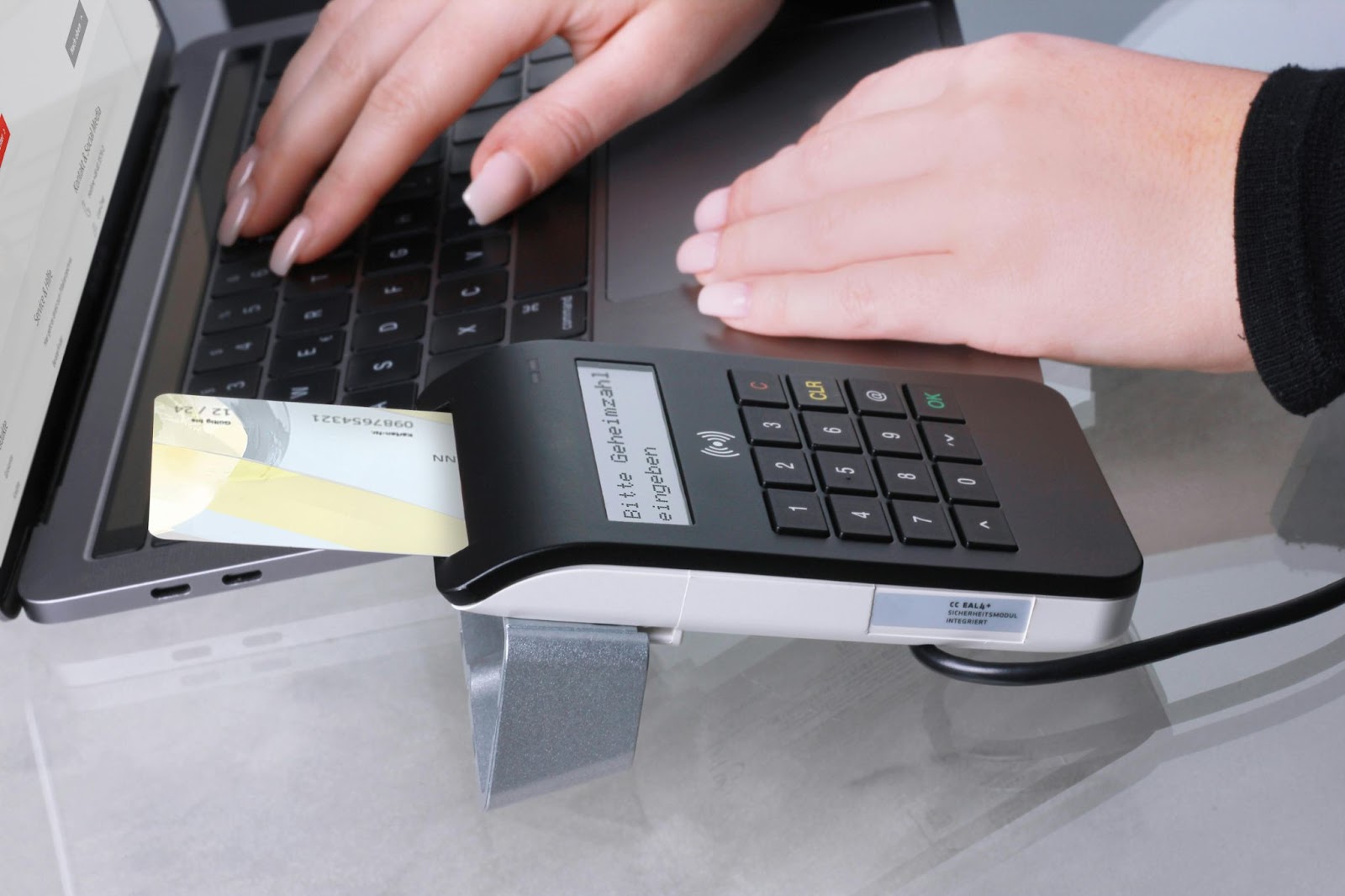 A close-up of a hand using a contactless payment device with a payment card inserted into the reader, attached to a laptop