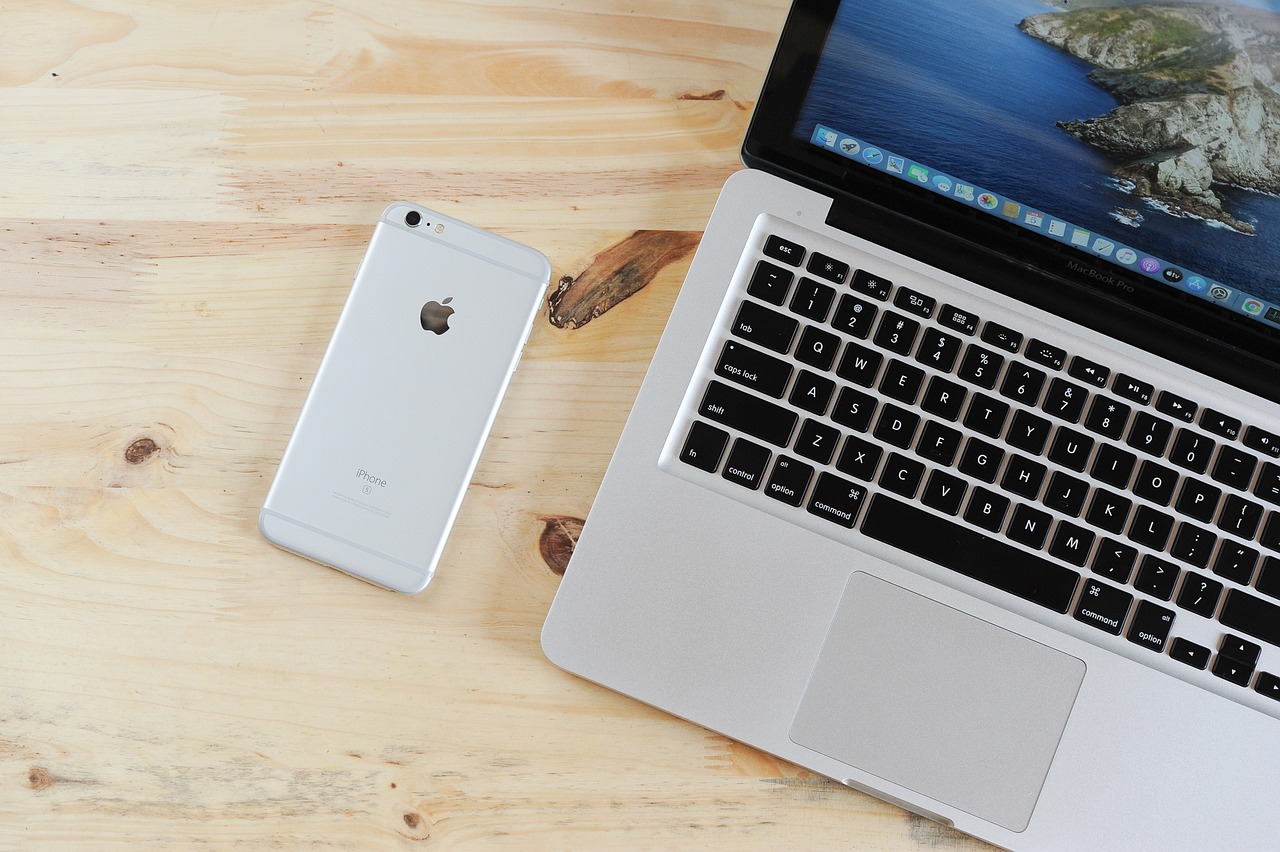 A photo of an iPhone and an open MacBook with a nature-themed wallpaper on a wooden desk