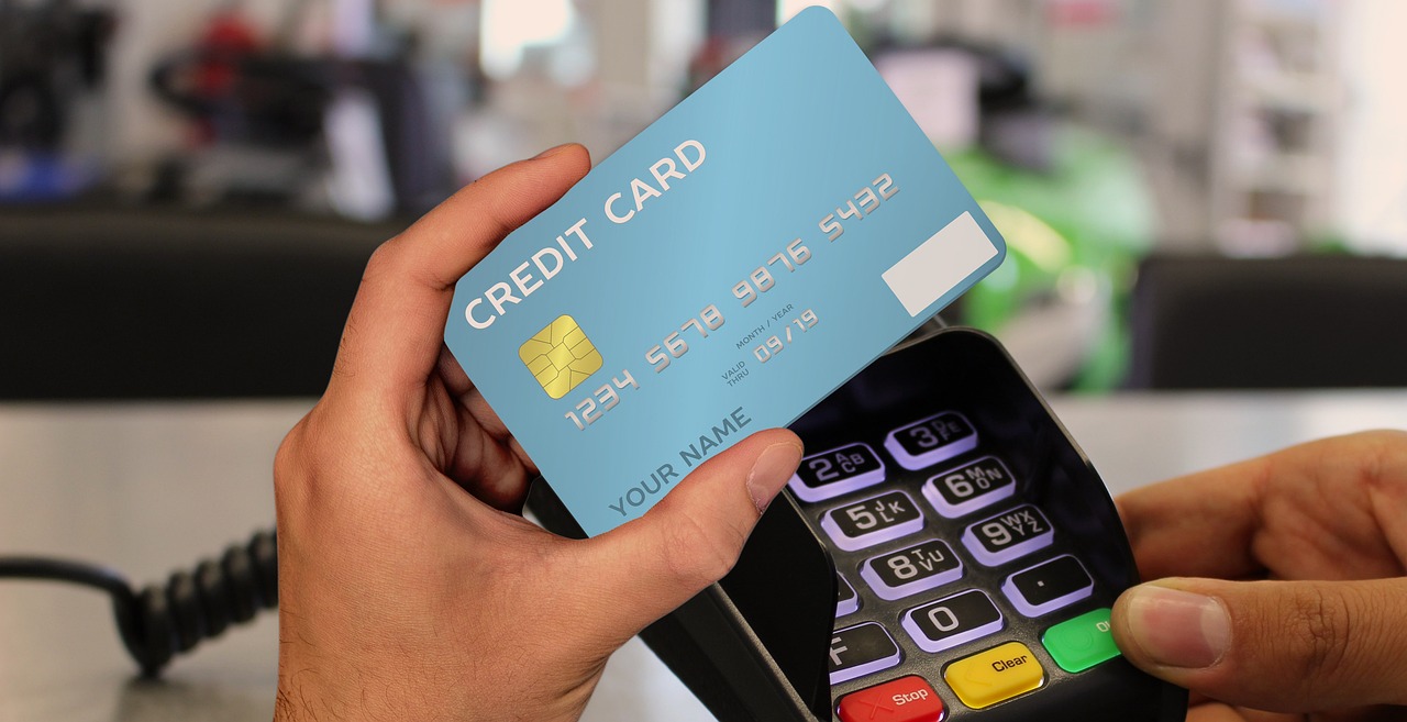 A photo of a hand holding a gray credit card over a payment terminal