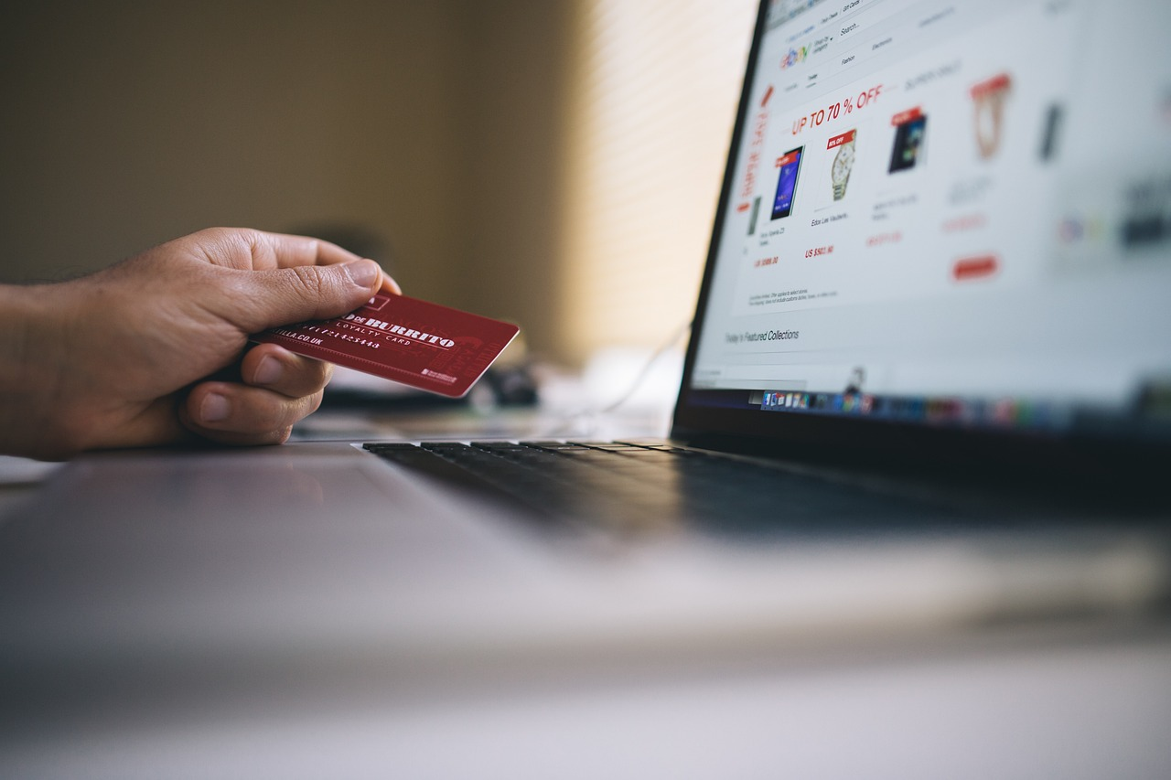 A cropped photo of a person holding a red payment card while browsing an online store on a laptop