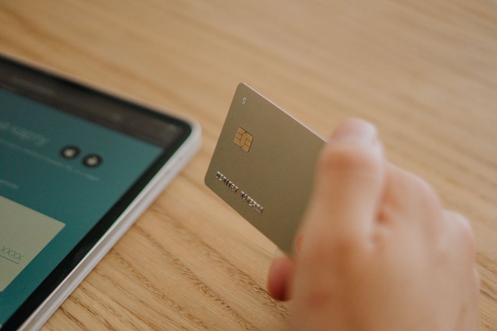 A close-up photo of a person holding a payment card with a smartphone in the background