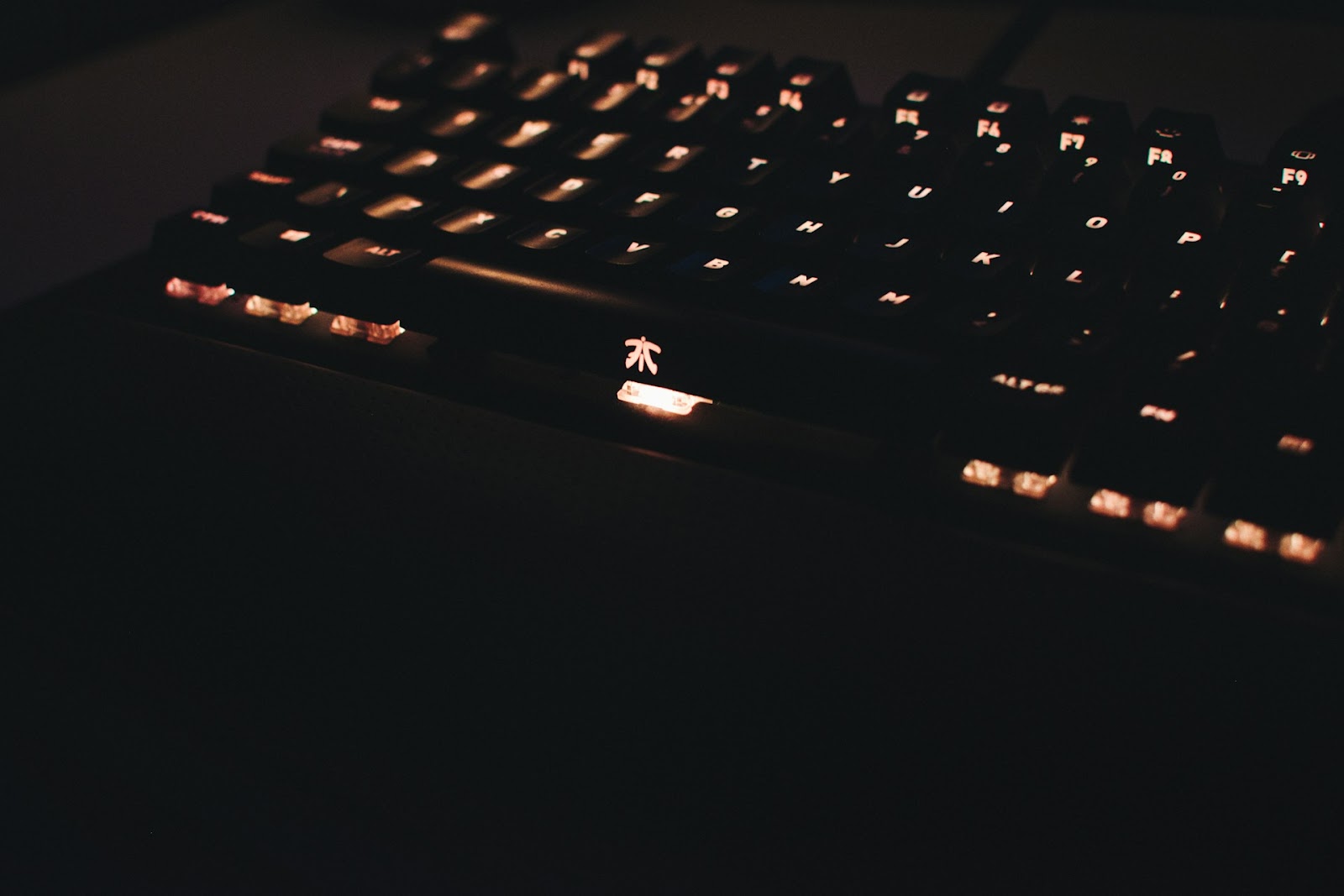A close-up of a black mechanical gaming keyboard with illuminated orange-red backlighting in a dark setting