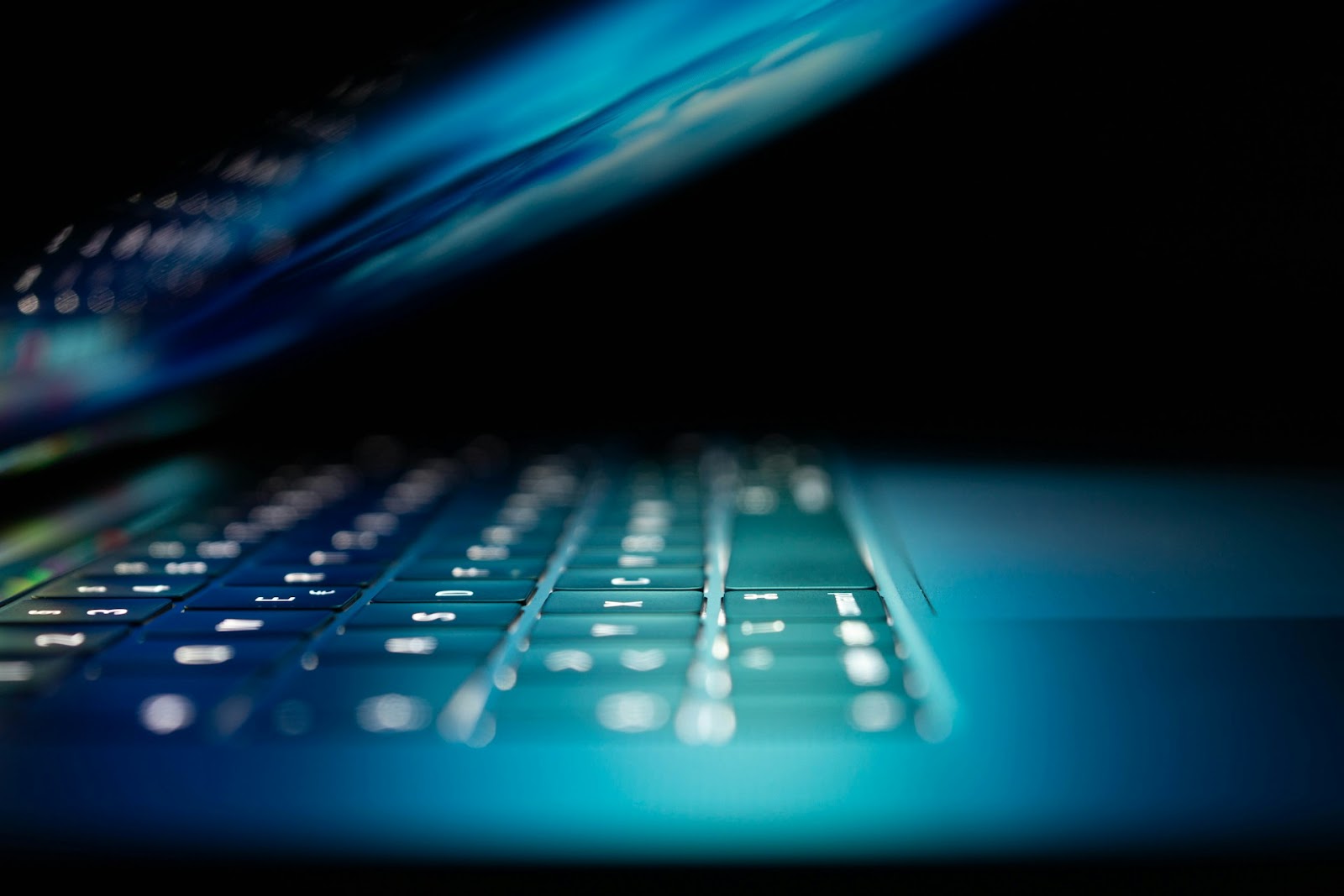 A close-up shot of a partially closed laptop with backlit keys in a dark room