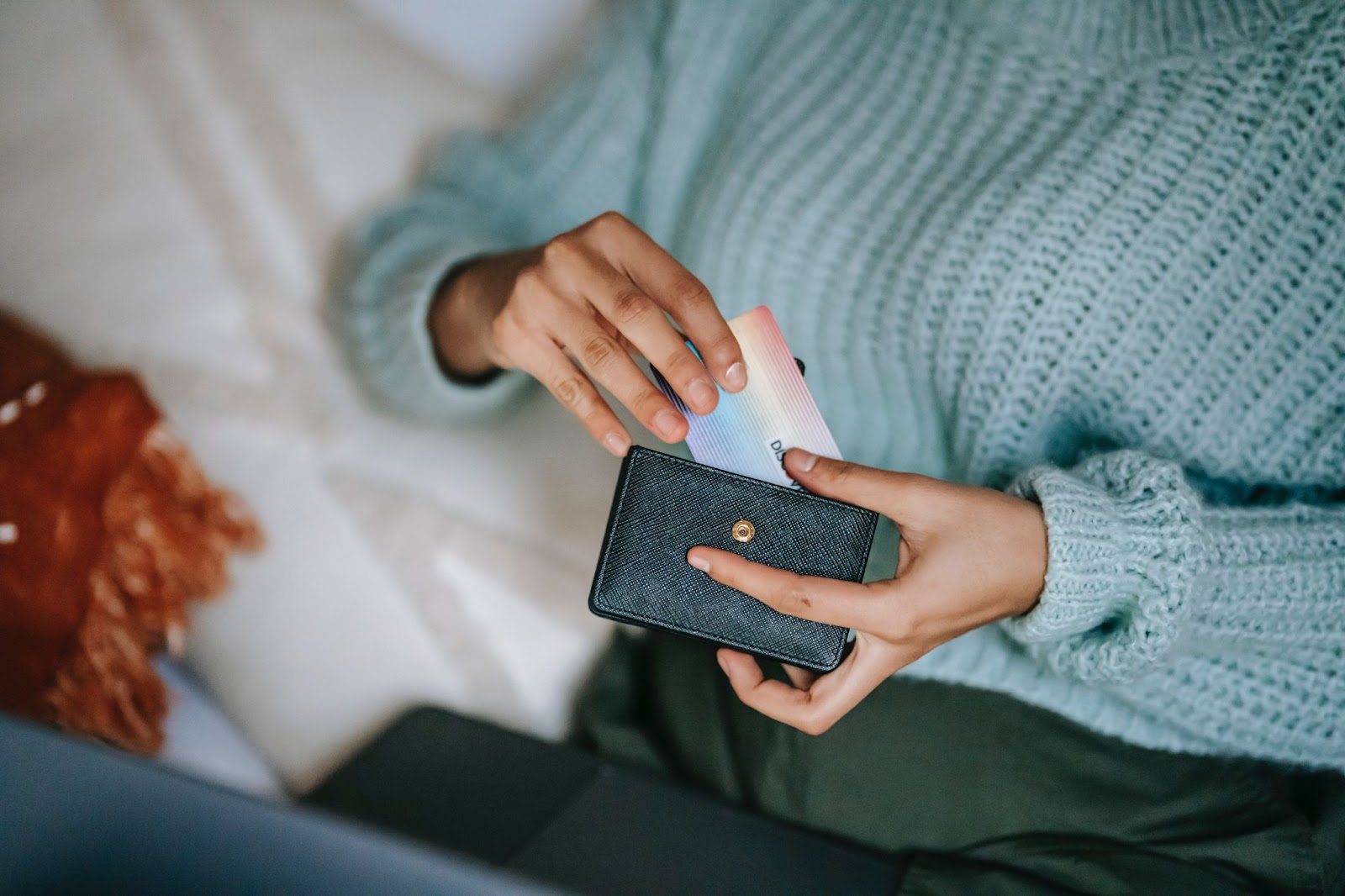 An image showing a person sitting at a laptop and pulling a card from a black wallet