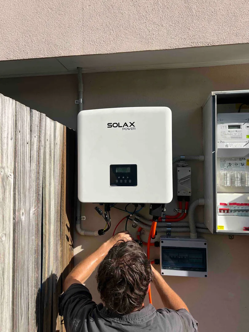 Person working on electrical wiring connected to a Solax Power inverter mounted on an exterior wall