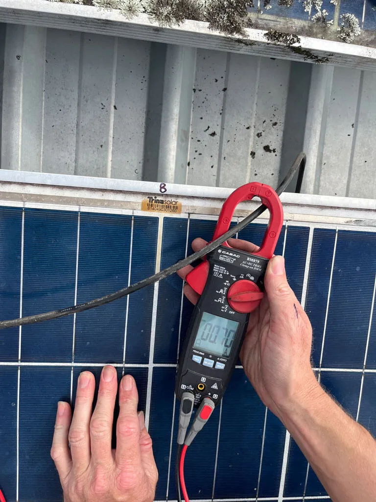 Hands holding a clamp meter testing the current on a solar panel