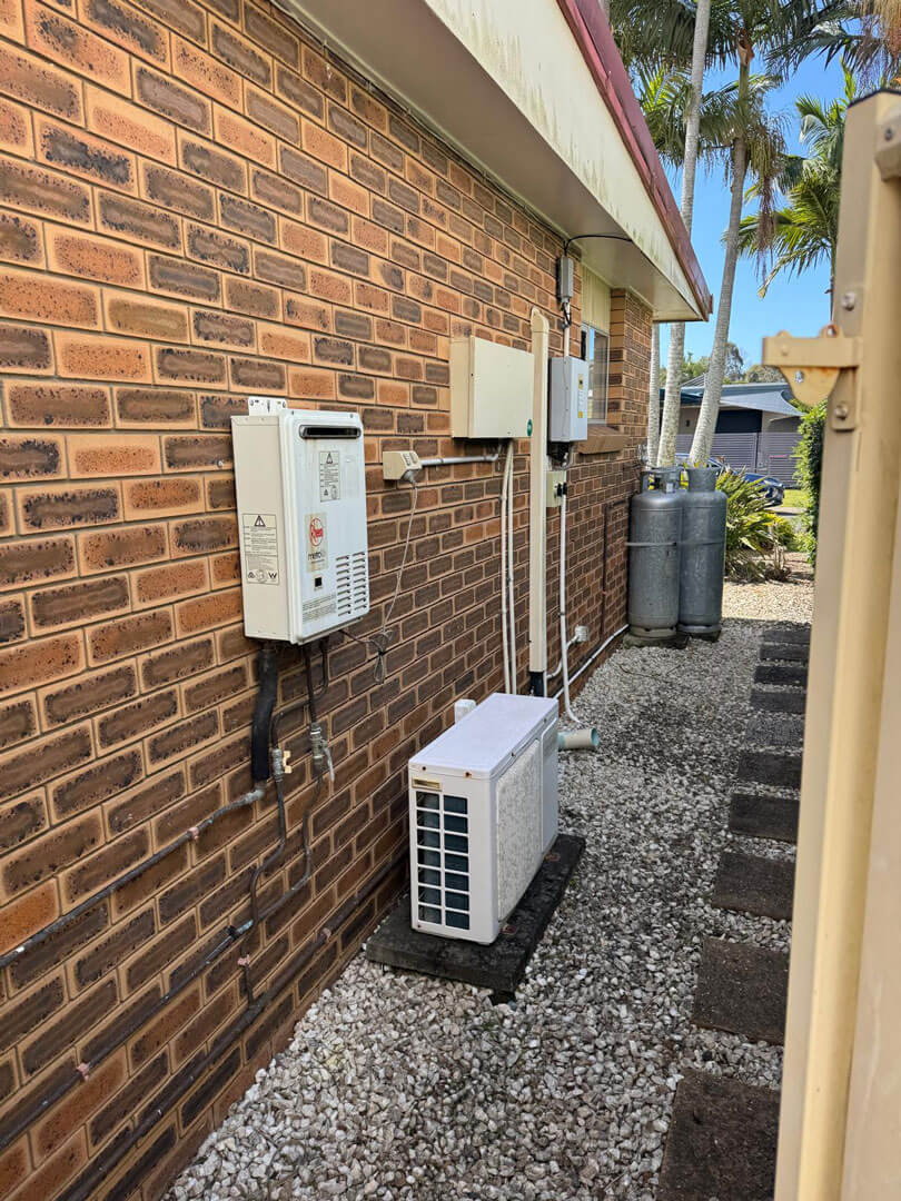 Electrical and air conditioning units installed on the exterior brick wall of a house with gravel and stepping stones on the ground