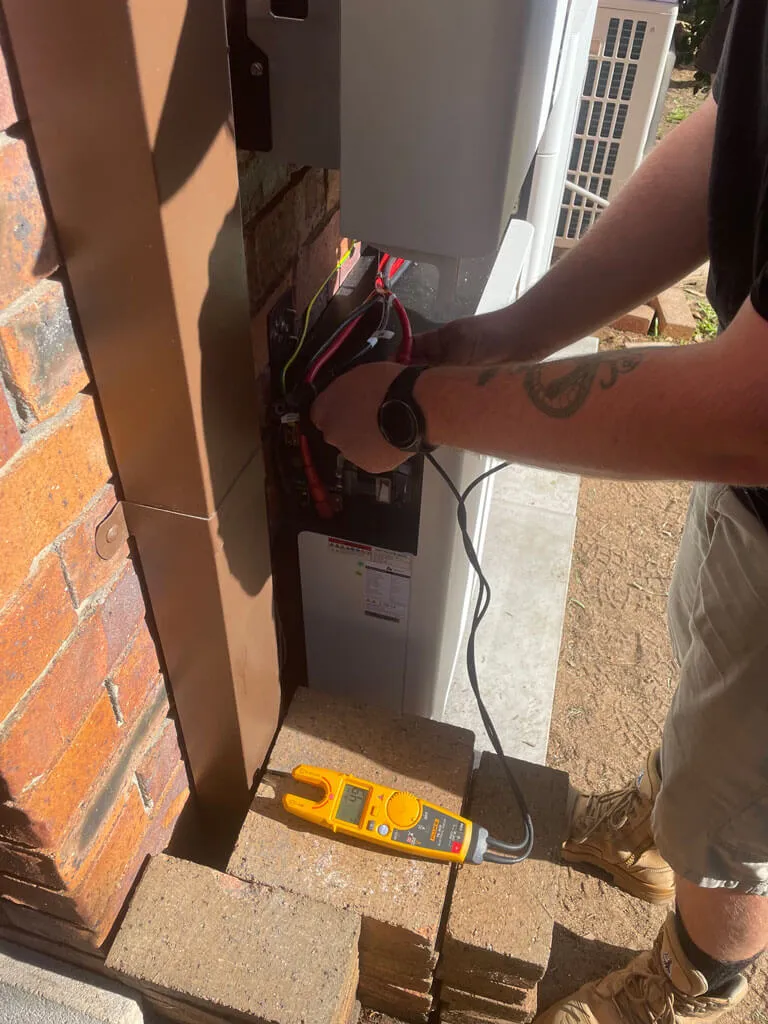 Person working on electrical wiring with a digital multimeter placed on bricks nearby