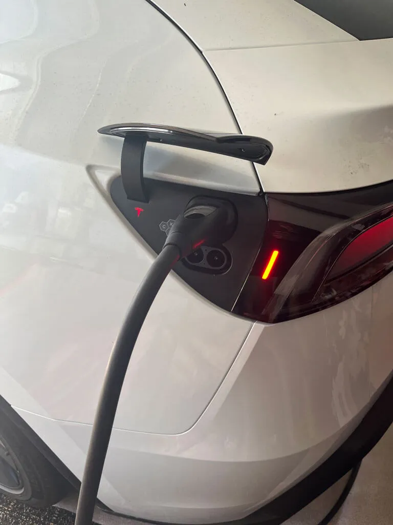 White electric car being charged with a cable plugged into the charging port