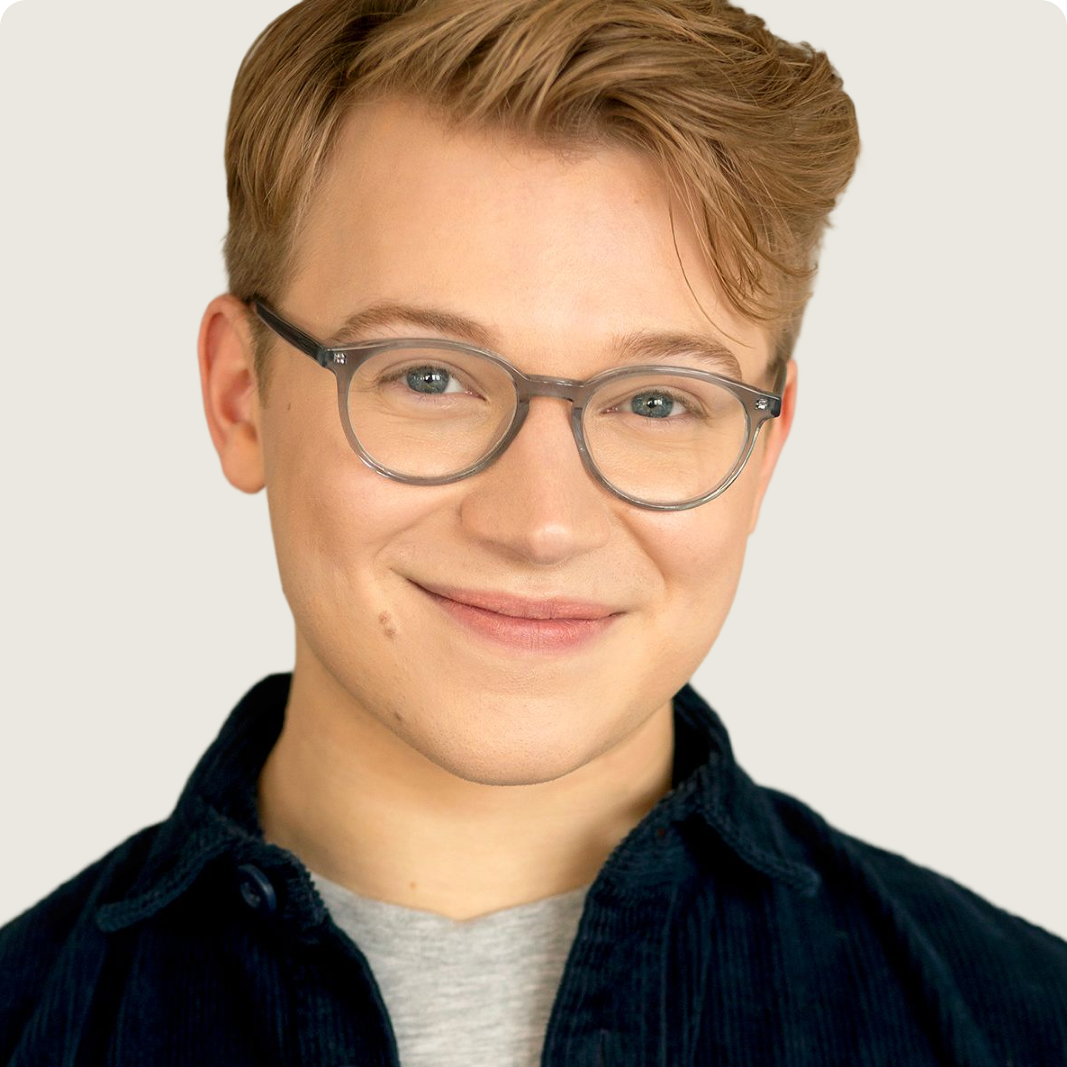 Young person with light brown hair, gray glasses, wearing dark shirt and smiling at the camera.