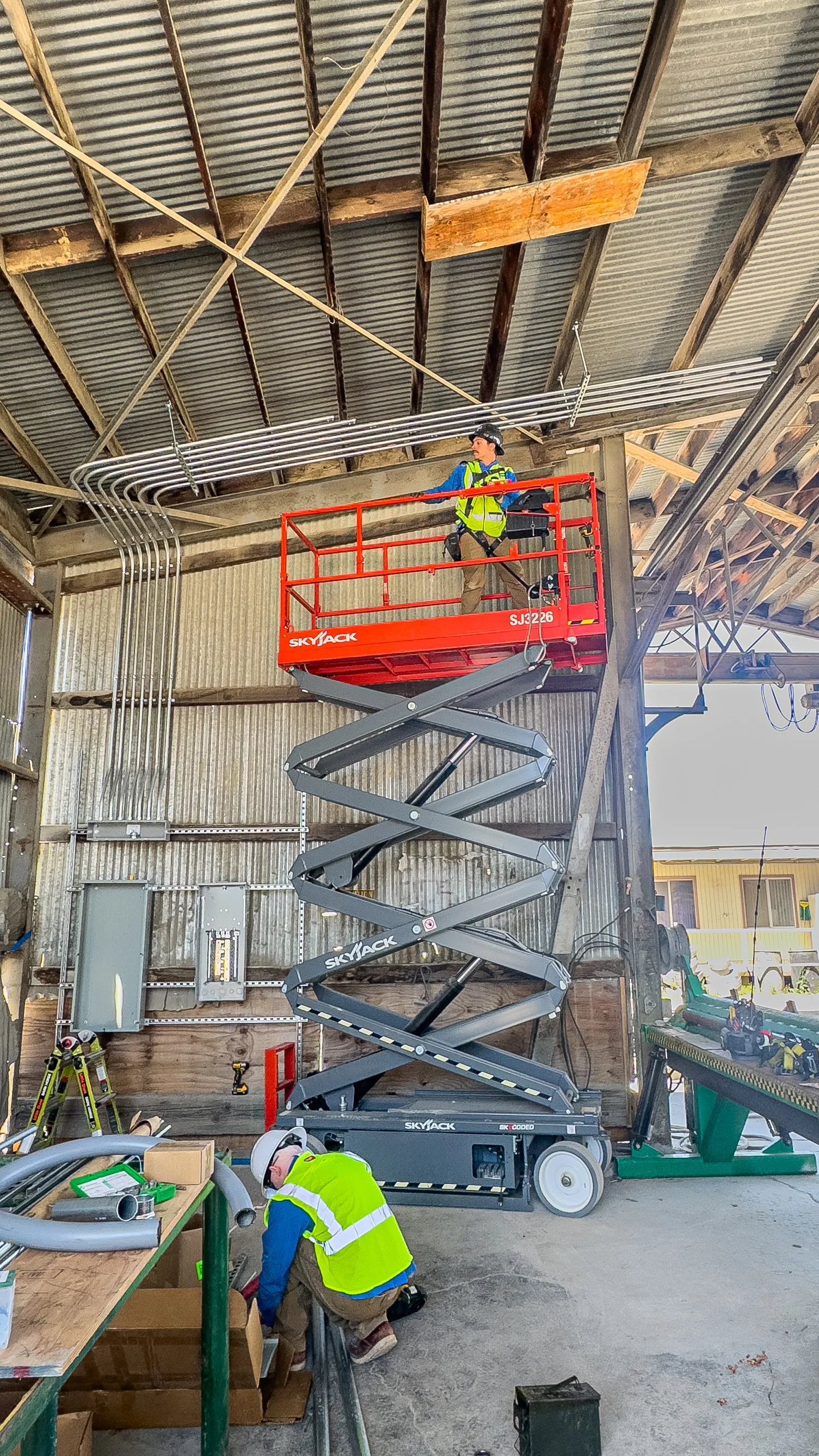 Elite Electrical electricians installing overhead conduit at an active Redding industrial fabrication facility.